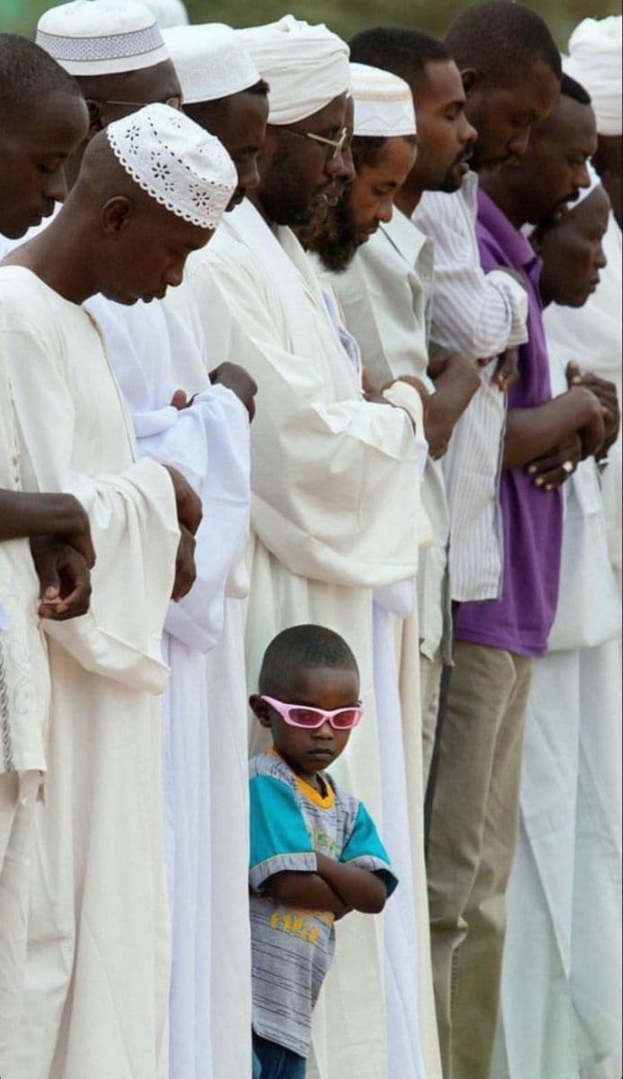 A boy in sunglasses among men at prayer